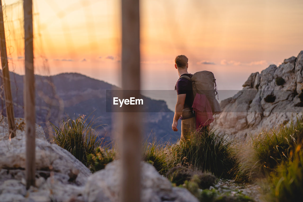 Lonely traveler stands on a viewpoint of a mountain during sunset