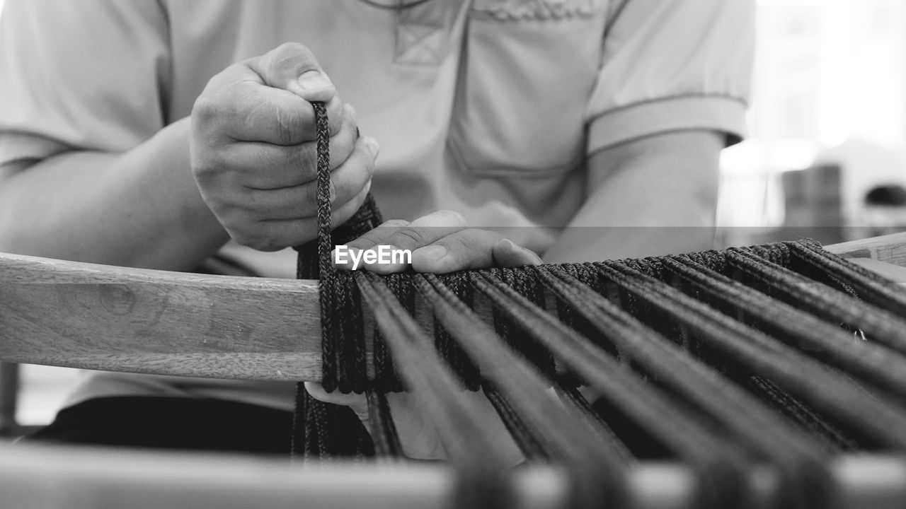 Midsection of woman weaving loom in workshop