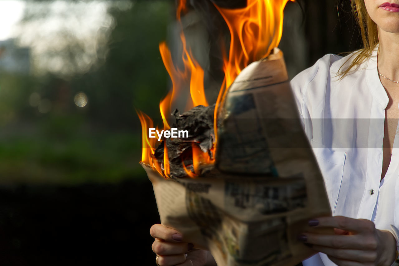 Midsection of woman holding burning paper outdoors