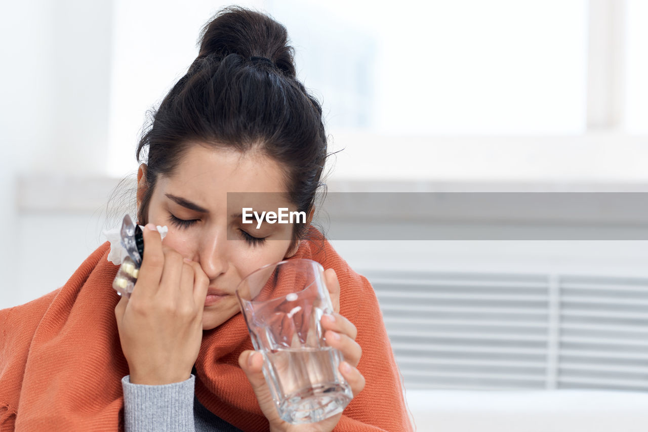 Sick woman holding medicine sitting at home