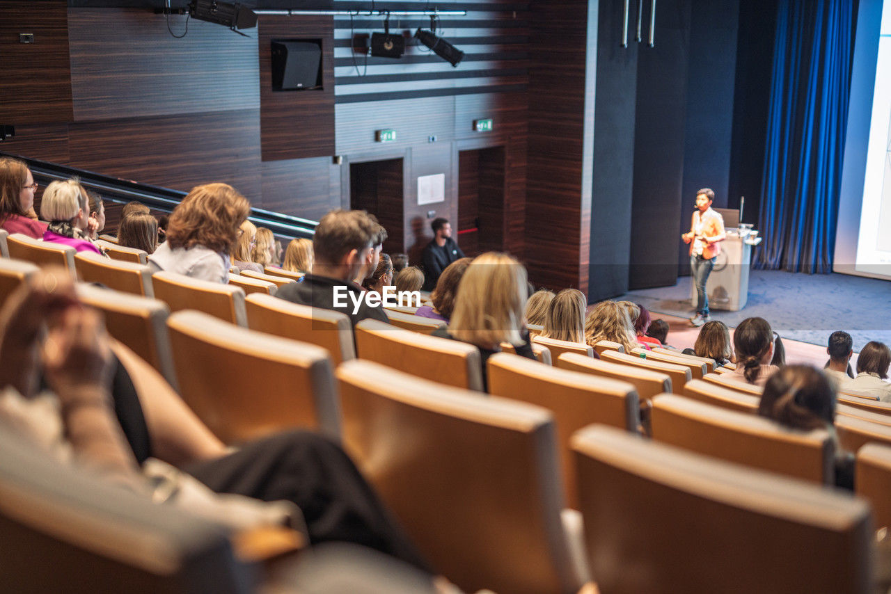 group of people, women, sitting, adult, education, auditorium, crowd, indoors, audience, men, student, female, learning, convention, child, school, young adult, large group of people, arts culture and entertainment, architecture, talking, teenager