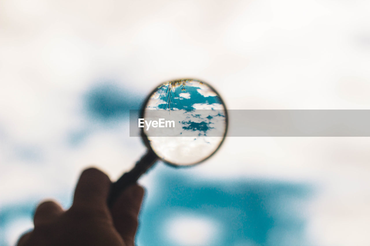 Magnifying glass pointing at cloudy blue sky