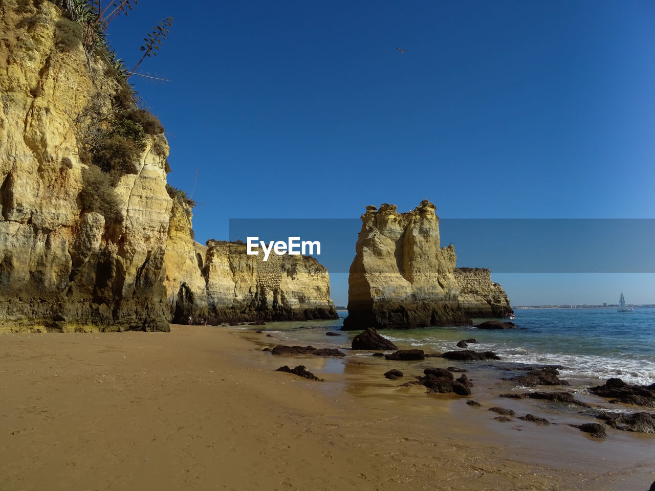 Rock formations on beach against clear blue sky