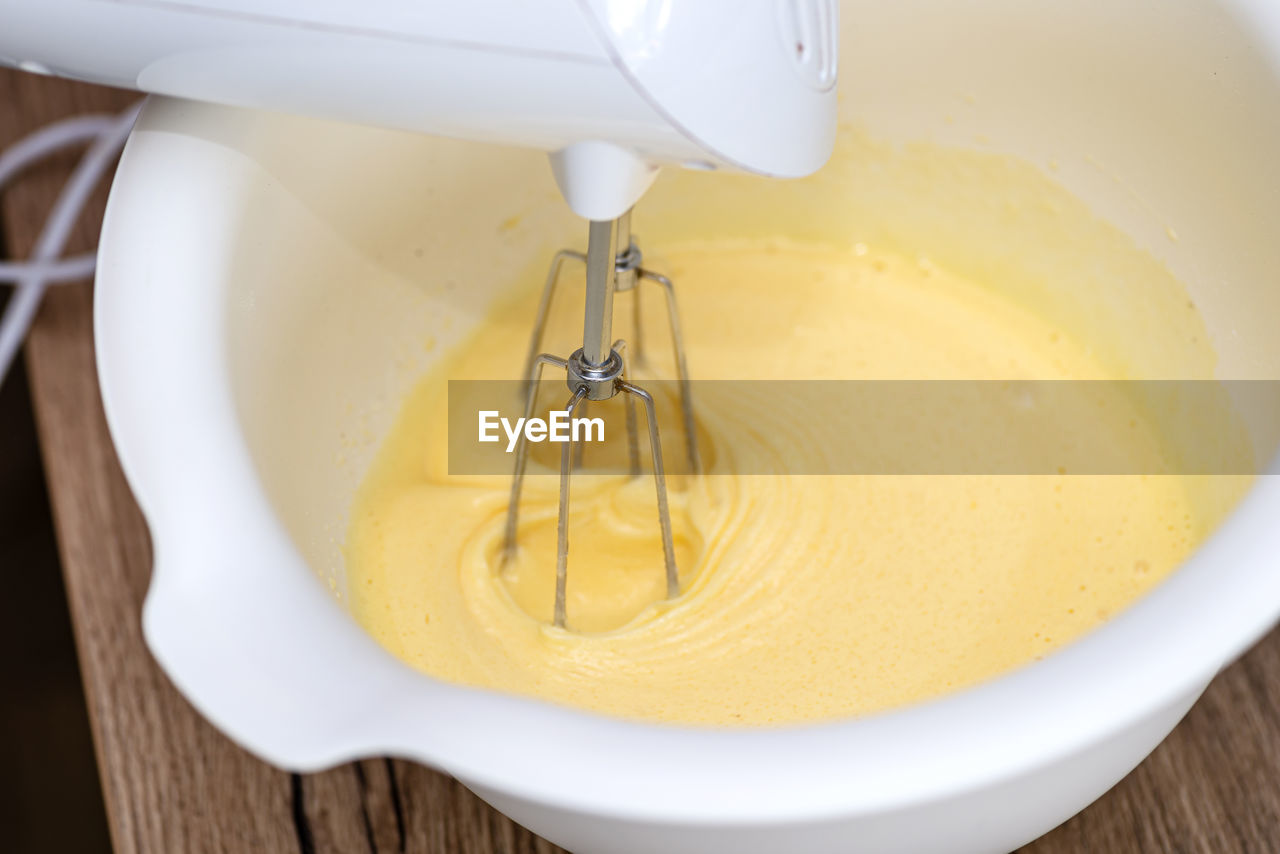 Kneading the dough using a hand mixer with a whisk, the dough is in a yellow liquid state.