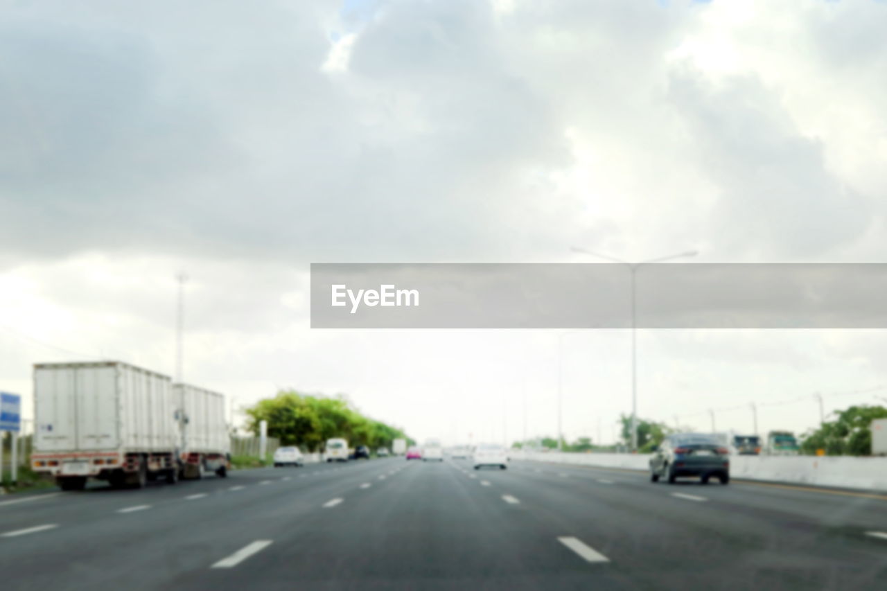 Vehicles on road against cloudy sky