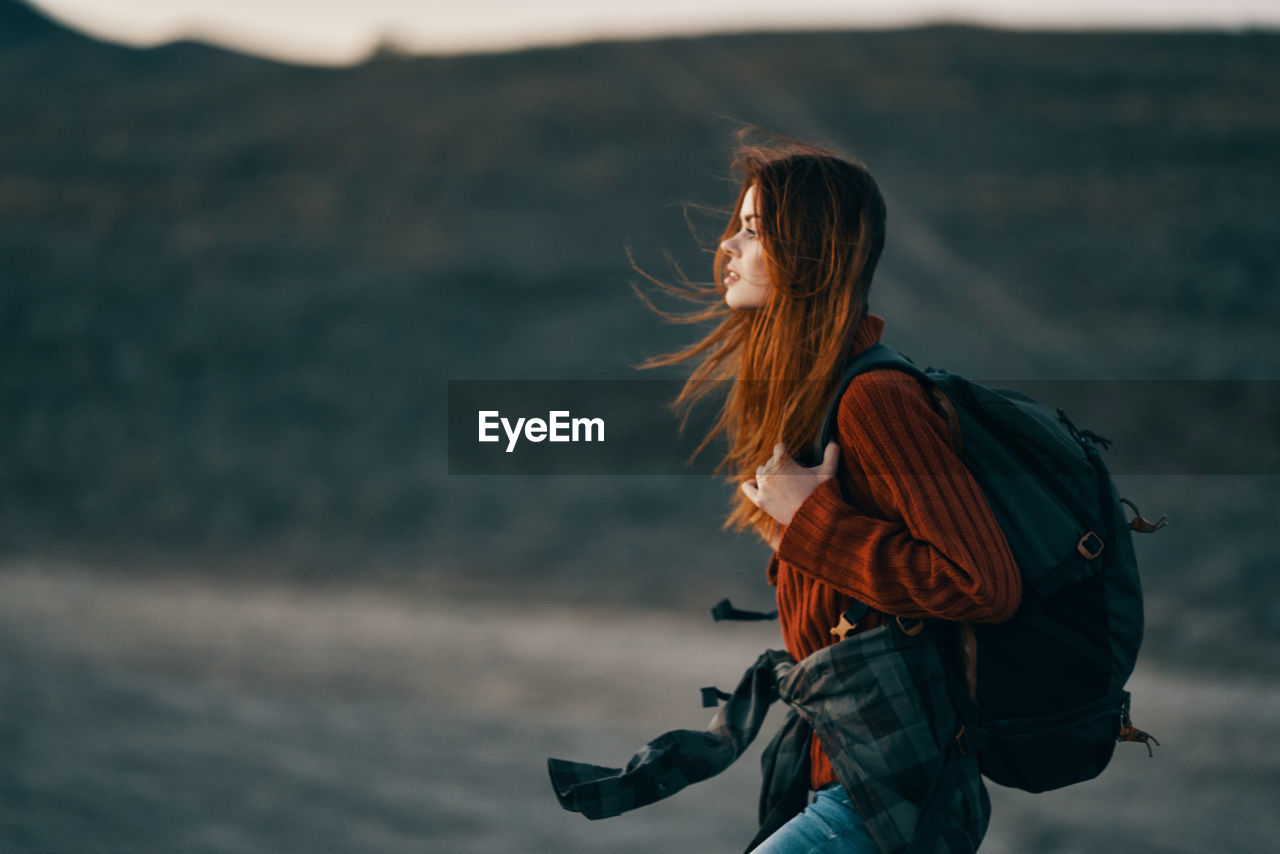 SIDE VIEW OF WOMAN STANDING AGAINST ORANGE SKY