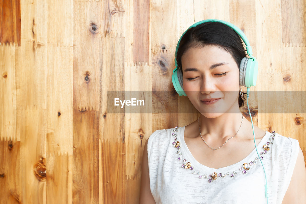 Woman listening to music against wooden wall