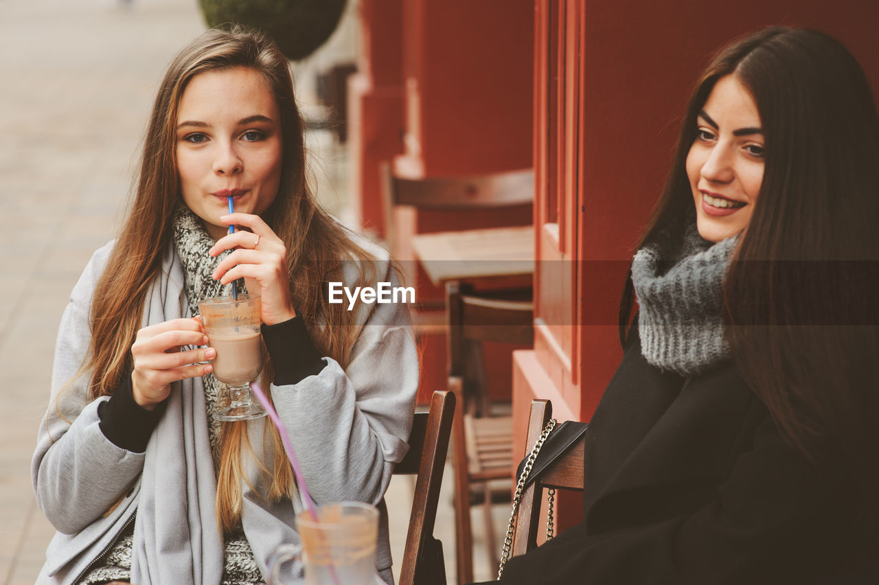 Female friends having drink while sitting at sidewalk cafe