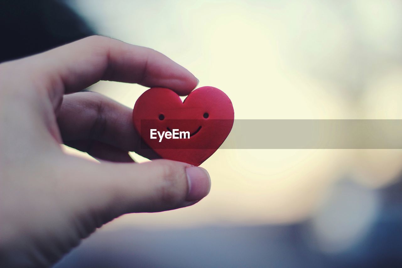 Close-up of human hand holding heart shape against sky during sunset