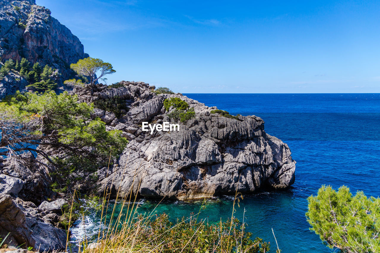 Scenic view of cliff by sea against blue sky