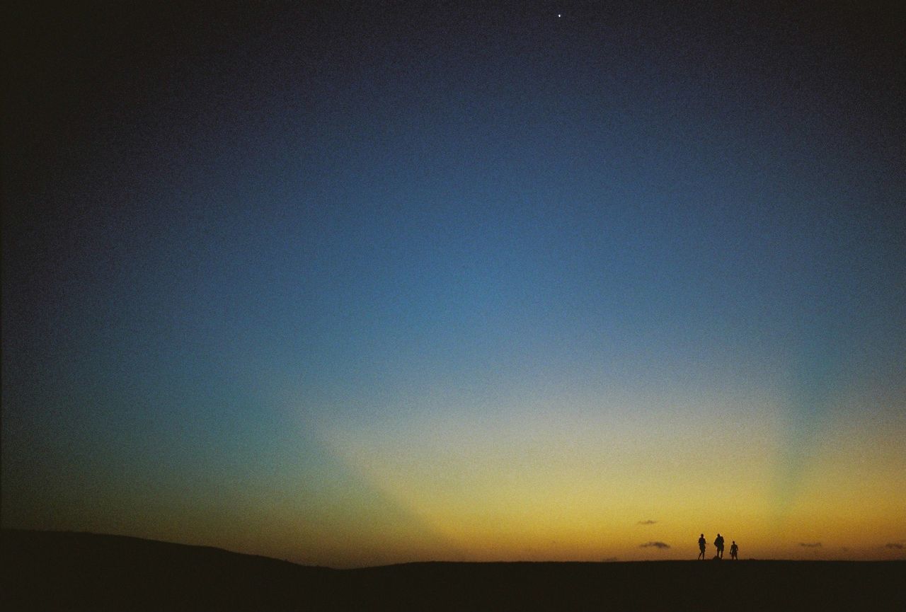 Distant view of silhouette men standing on landscape at sunset