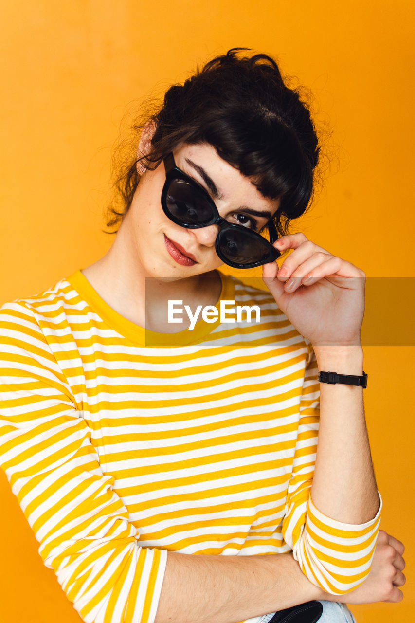 Portrait of young woman wearing sunglasses against orange background