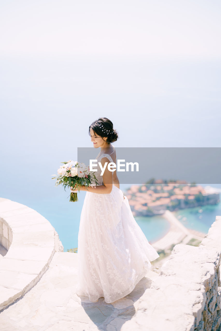 Woman standing on rock by sea against sky