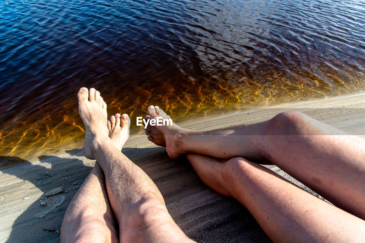 Legs of a man and a woman by the river against reddish water in the background. 