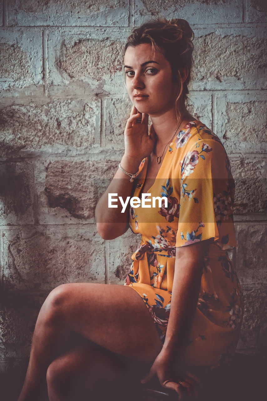 Beautiful young woman sitting against wall