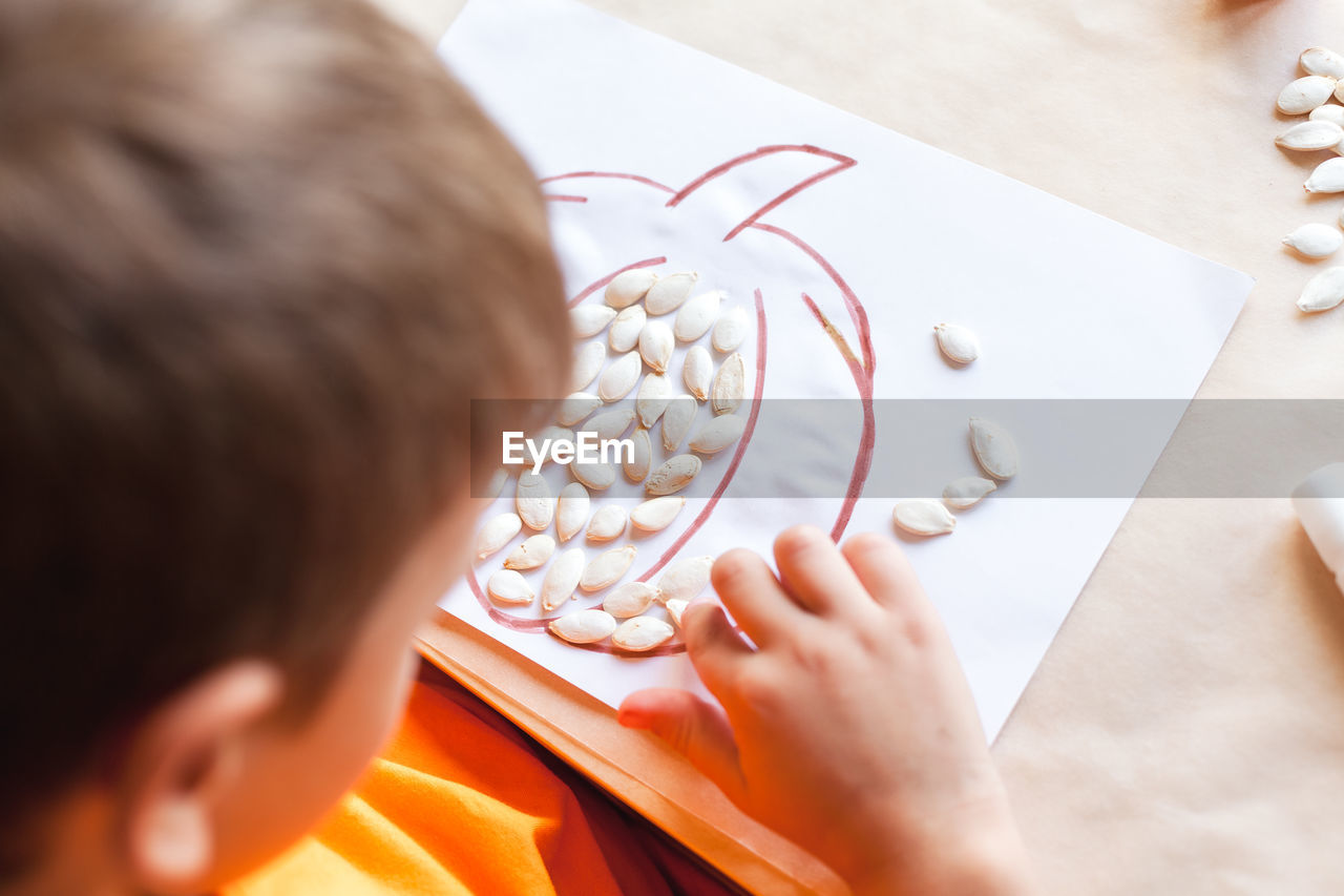 Cute boy making pumpkin from seeds on paper, halloween diy concept. step by step instruction. step 2