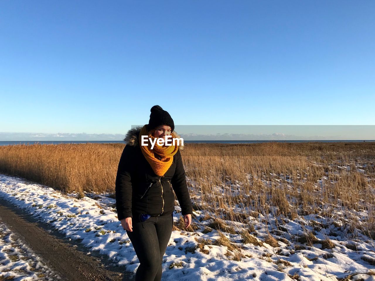 Smiling young woman walking on field against blue sky during winter