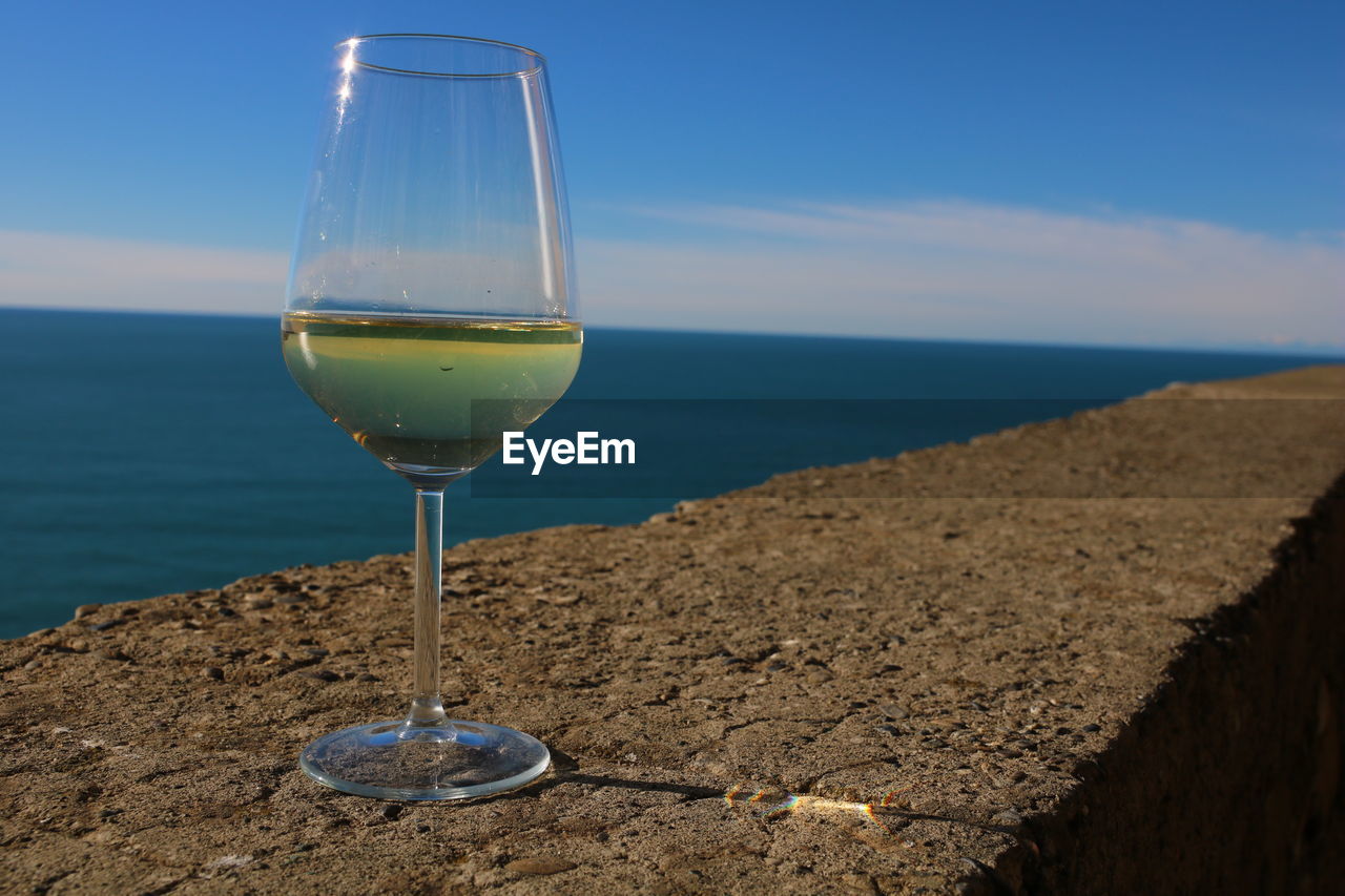 Close-up of wine glass on beach against sky