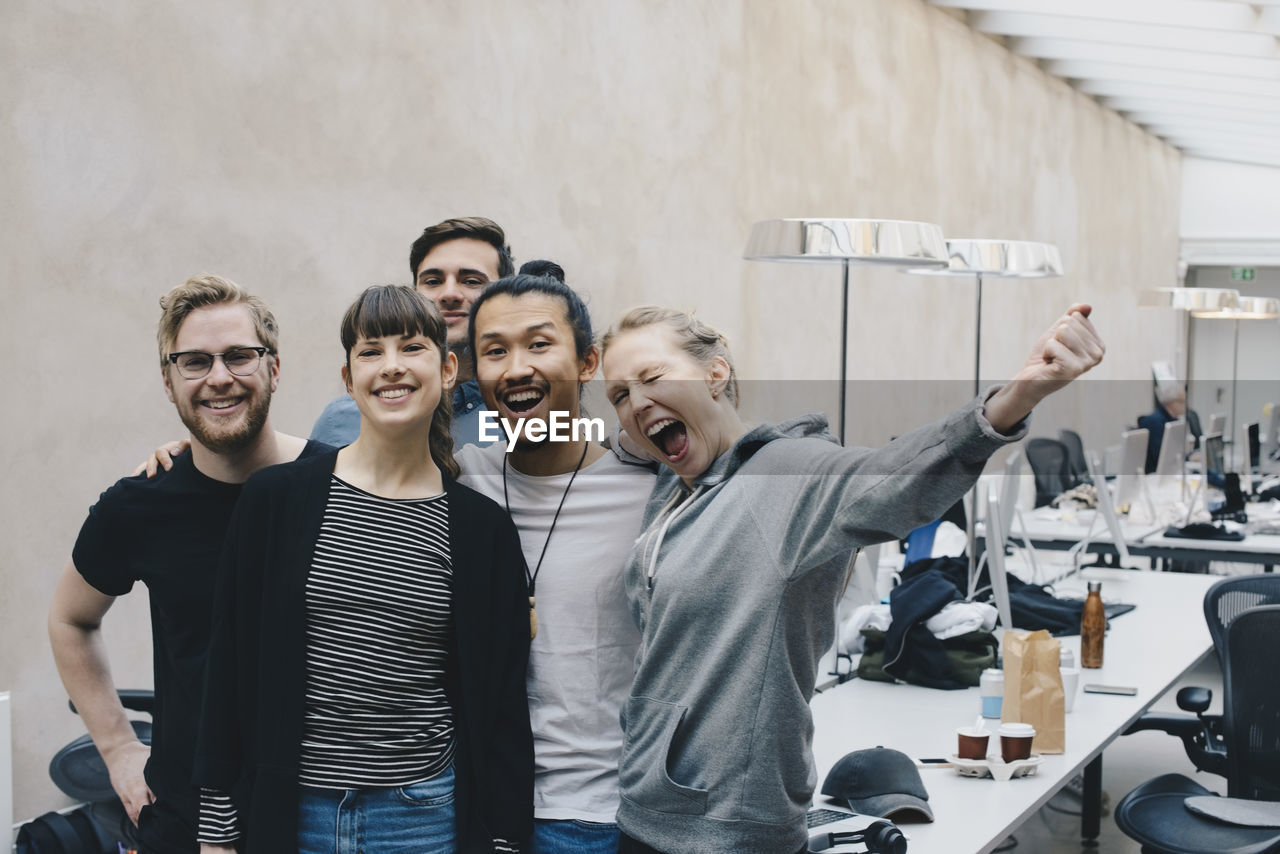 Excited female computer programmer screaming while standing with colleagues in office