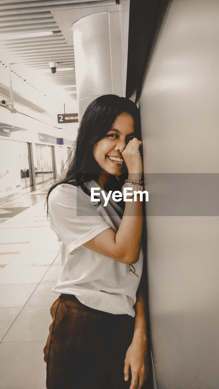 Portrait of smiling woman standing by wall