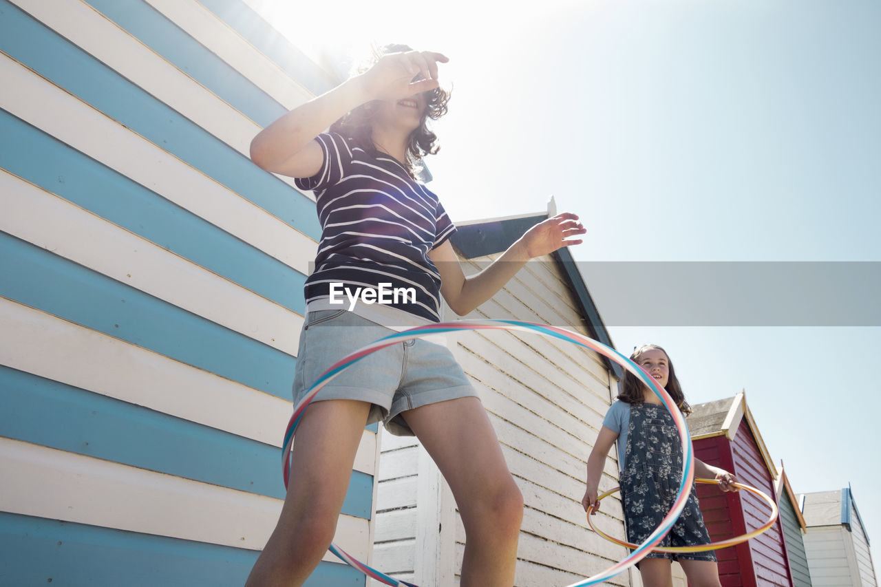 Friends spinning hula hoop against beach huts on sunny day during vacation