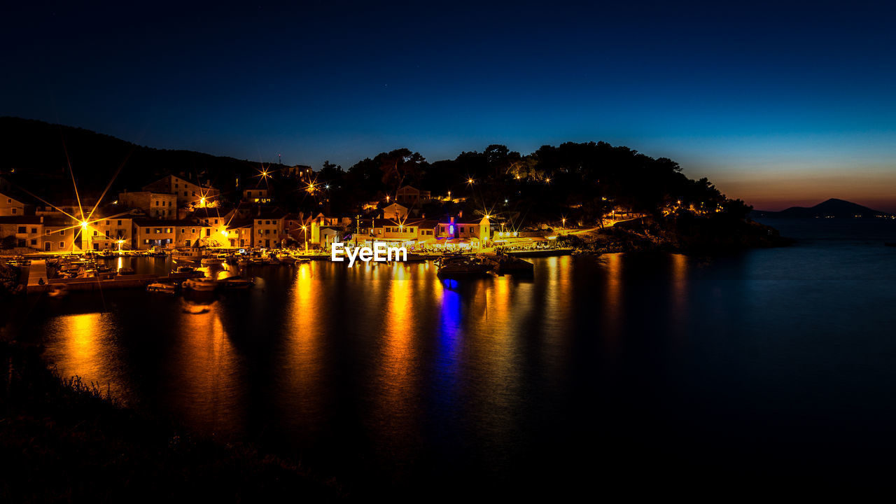 Illuminated buildings by sea against sky at night