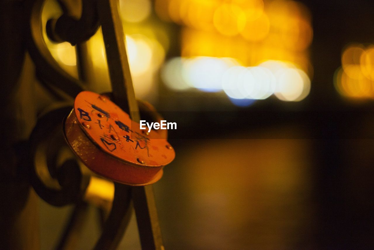 Close-up of love lock hanging in illuminated city at night