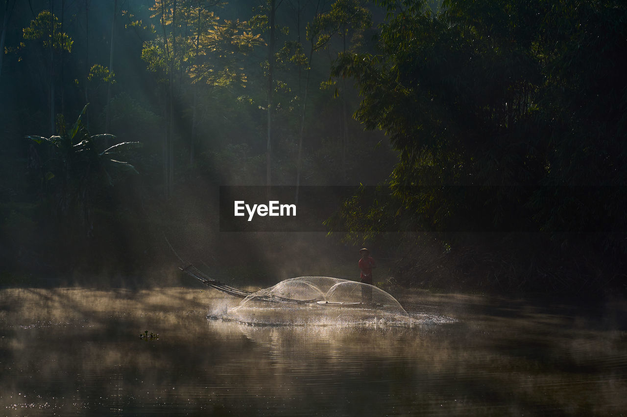 A fisherman is casting a fishing net to catch fish in the freshwater lake on 12 june 2021