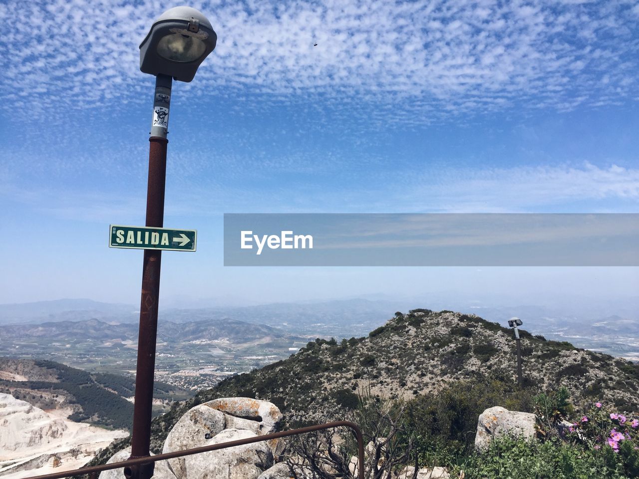 Low angle view of road sign on street light with mountain in background against blue sky