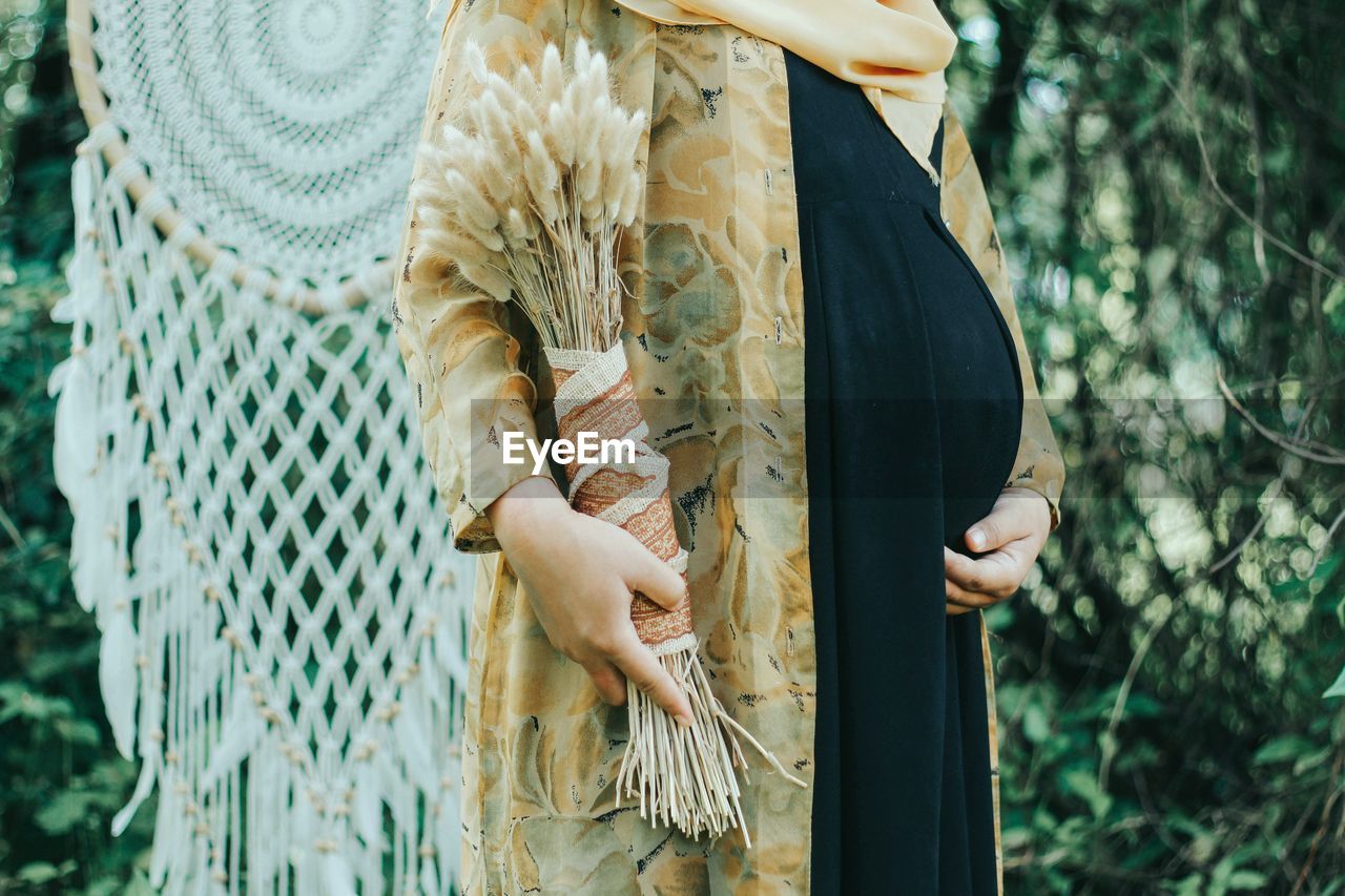 A pregnant woman is pictured holding a bouquet of beautiful dried flowers