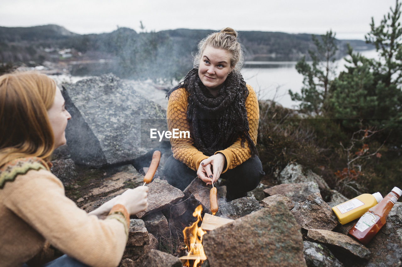 Women preparing hotdogs over campfire