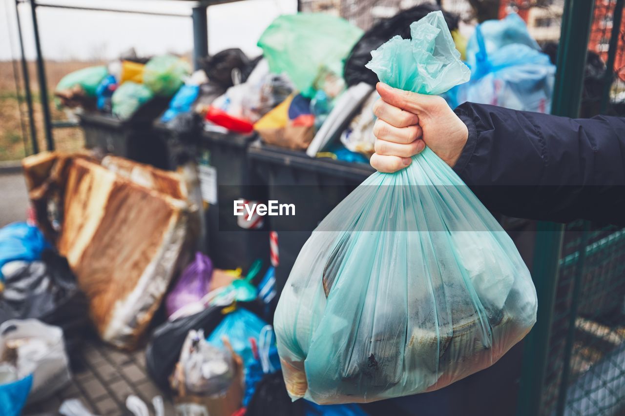 Cropped hand holding bag against garbage can