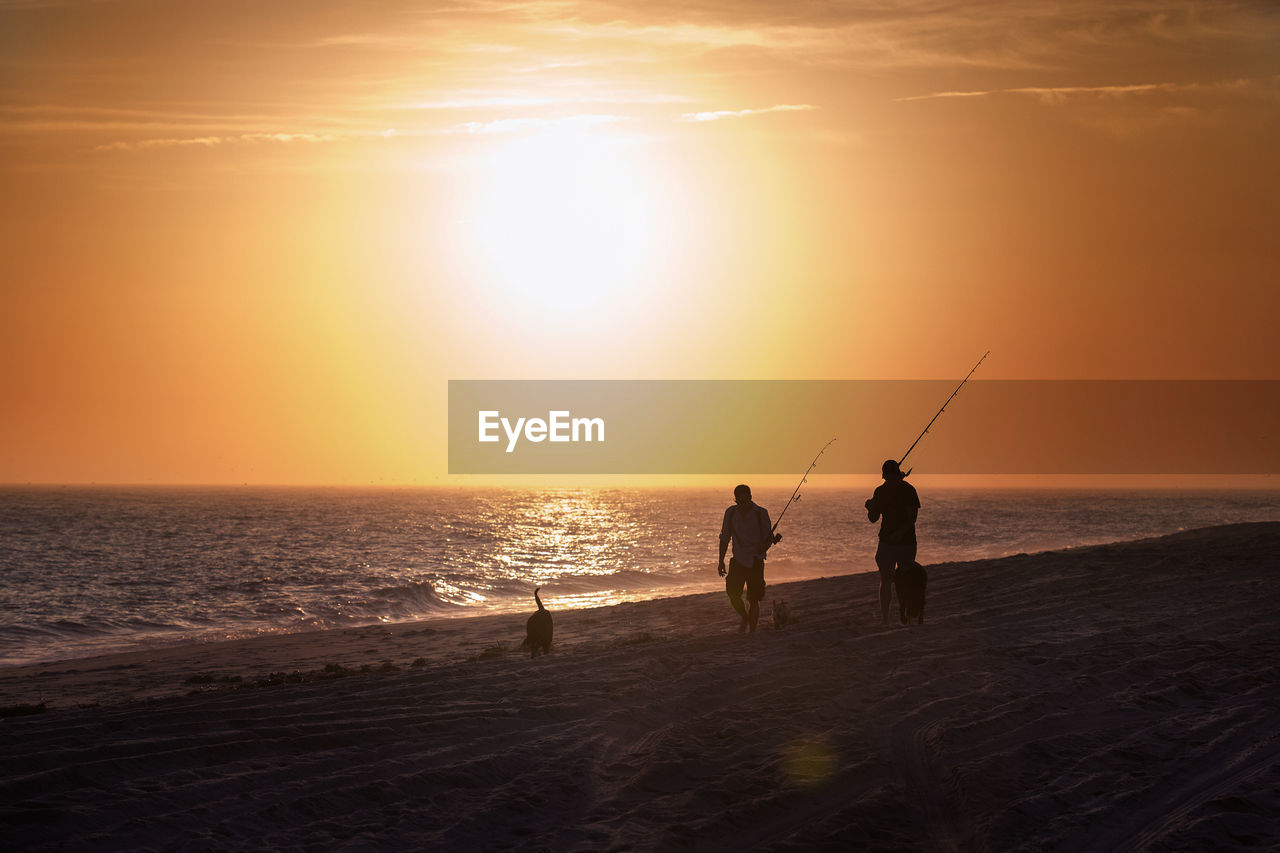 Silhouette men fishing at beach against sky during sunset