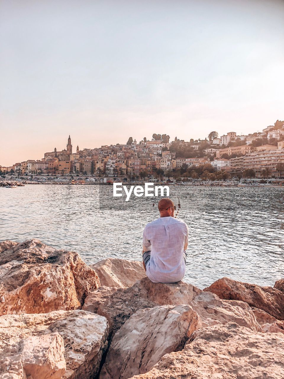 Rear view of man sitting on rock at sea against sky