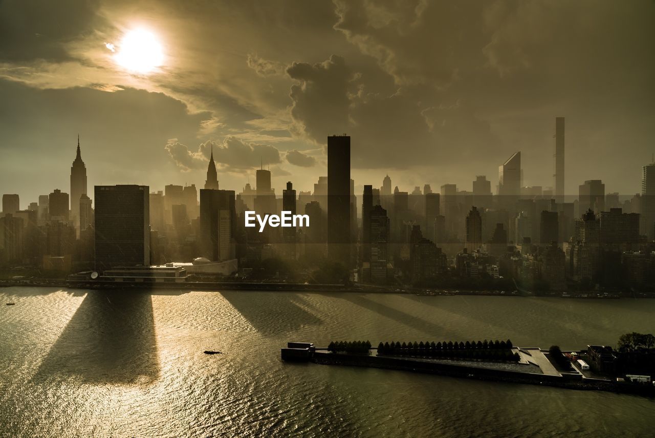 Skyscrapers in manhattan by east river against sky during sunrise