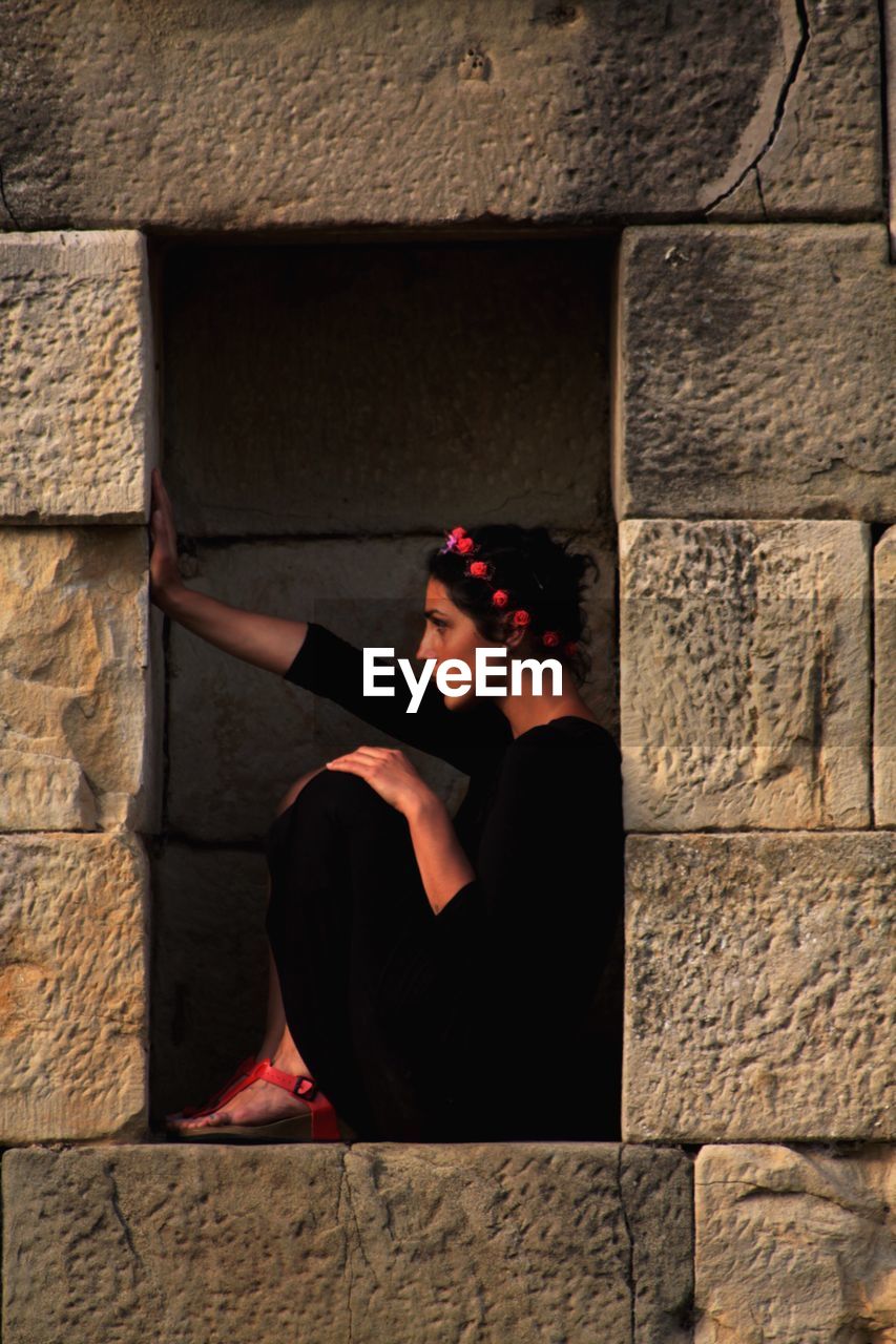 Side view of young woman sitting amidst walls