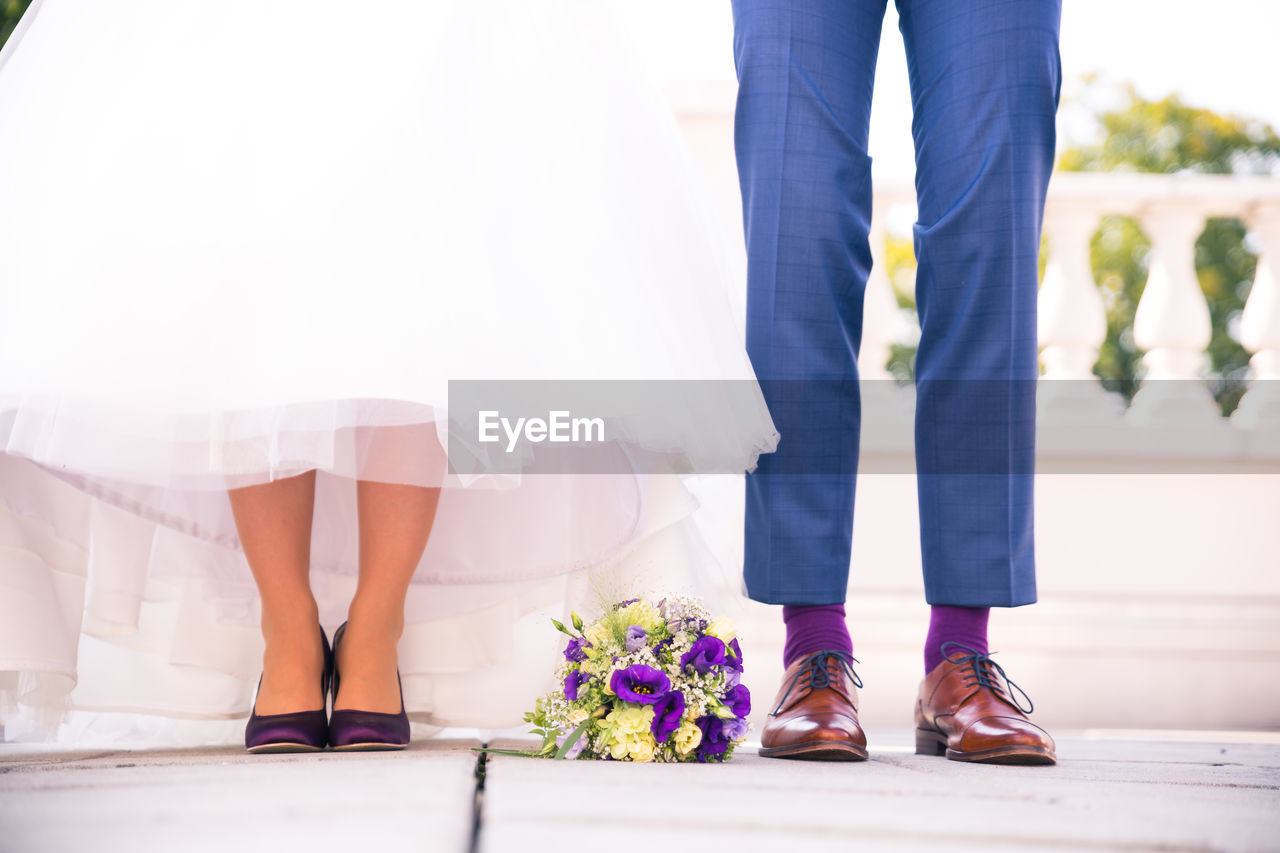 Low section of bride and groom with flower bouquet standing on floor