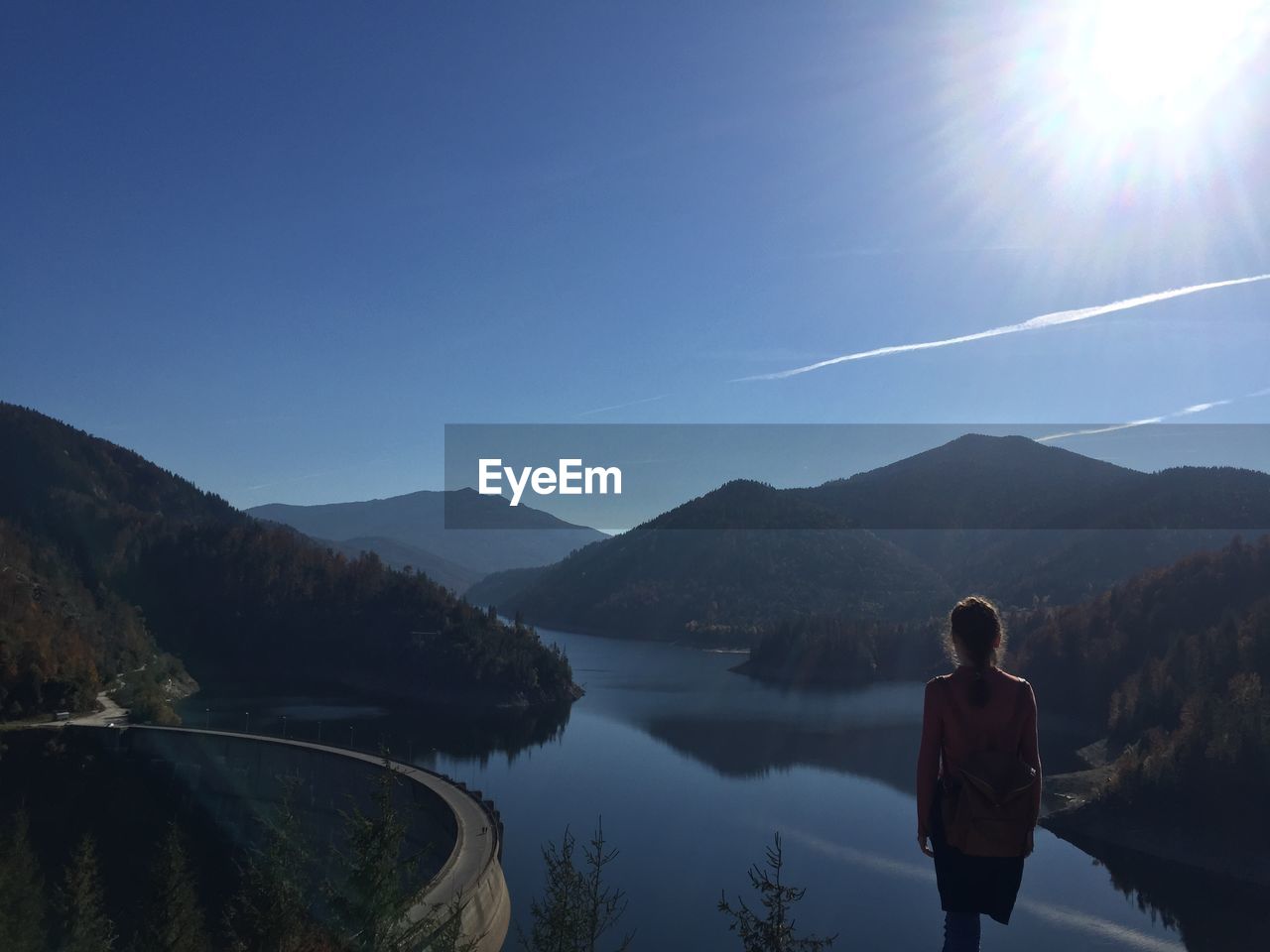 Rear view of woman standing on lake amidst mountains against sky