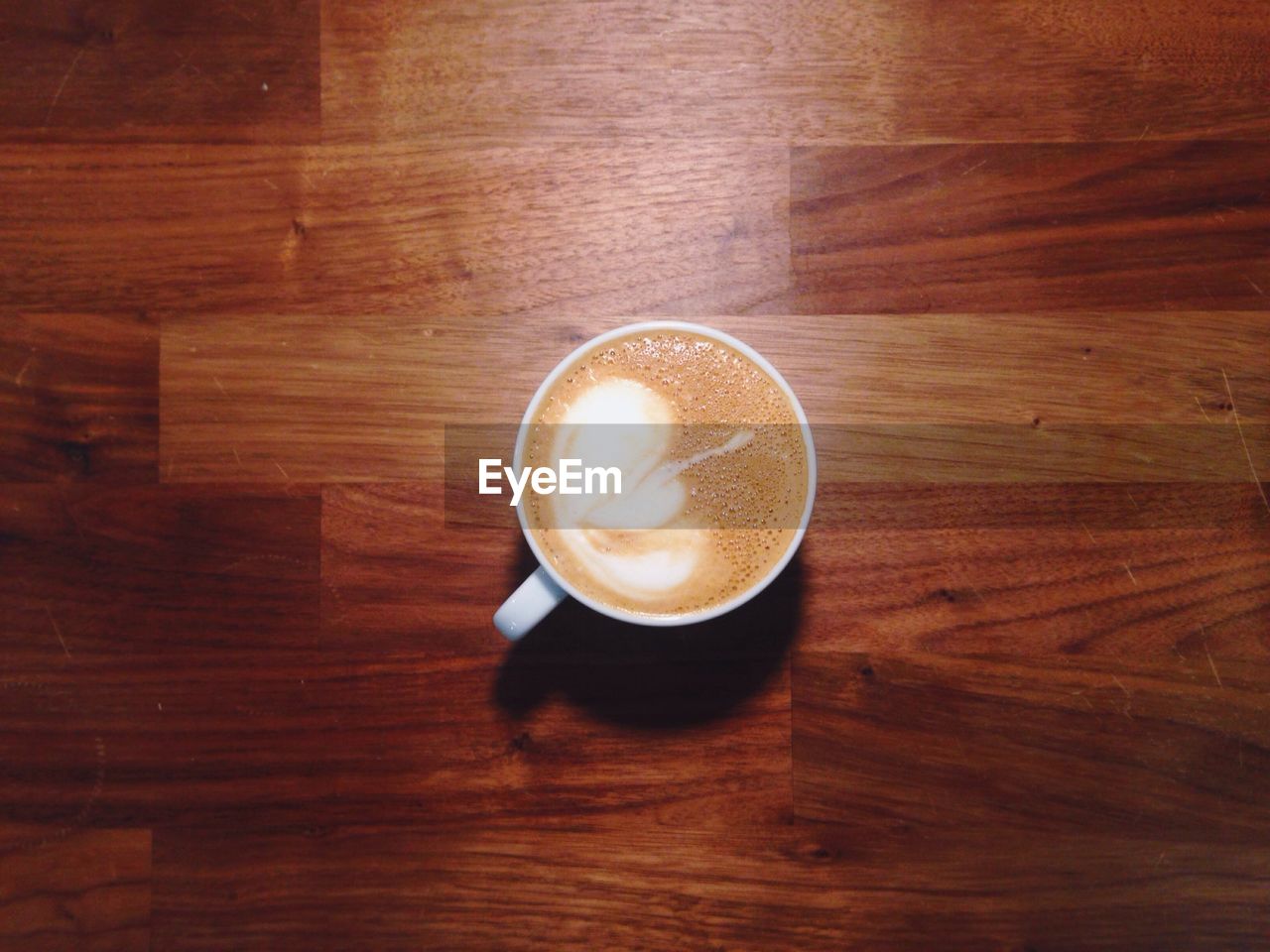 High angle view of coffee with froth art on hardwood floor