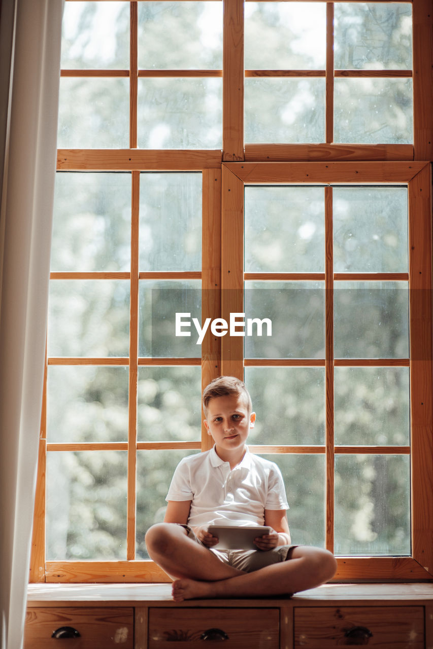 Full length of man sitting on table at window