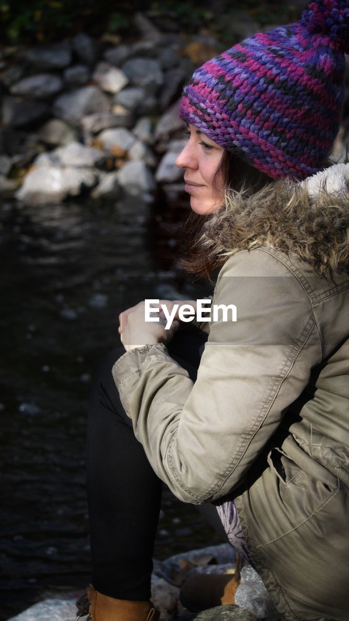 Side view of woman wearing warm clothing sitting by lake