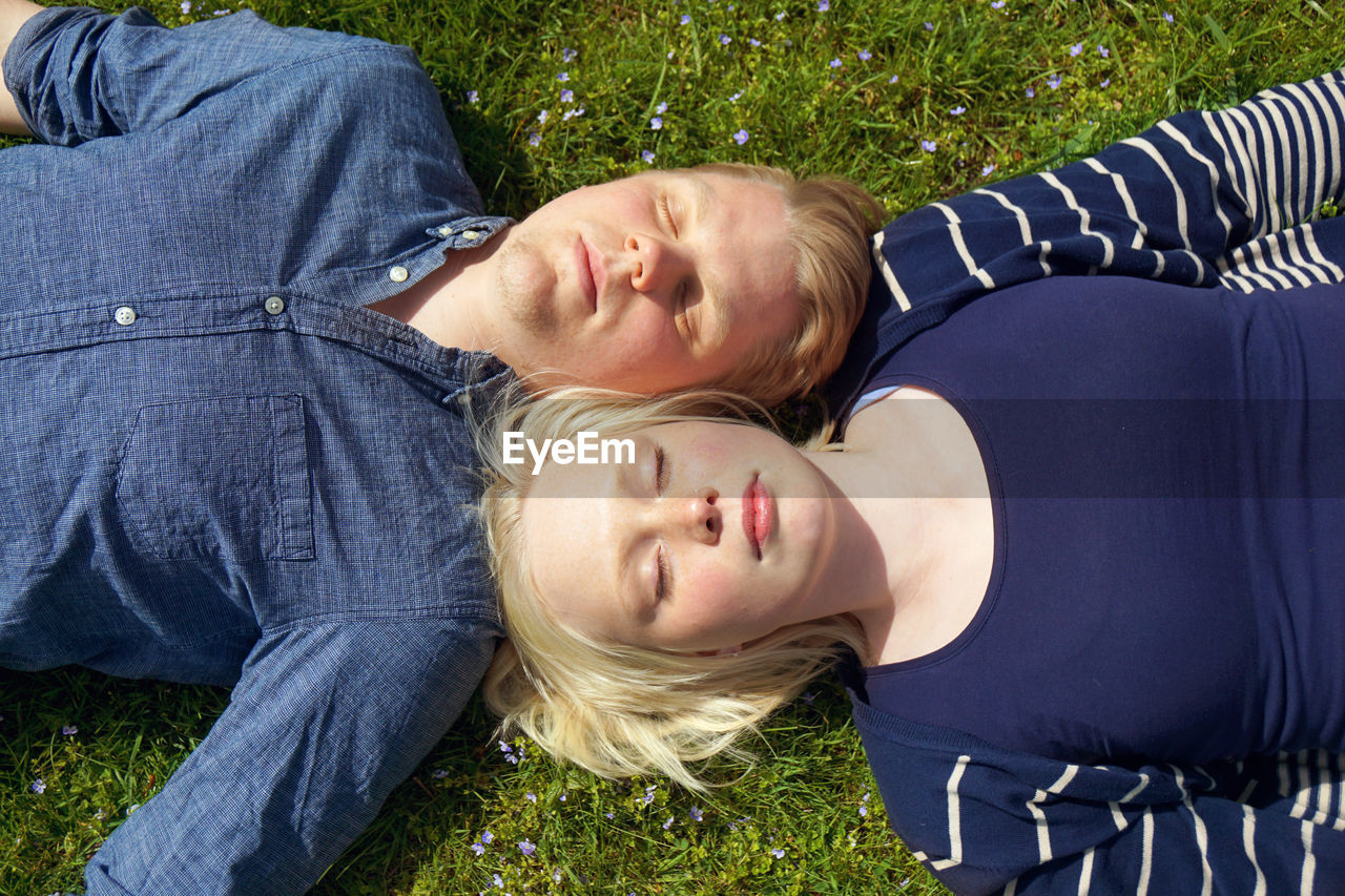 High angle view of couple with eyes closed lying on grass during summer