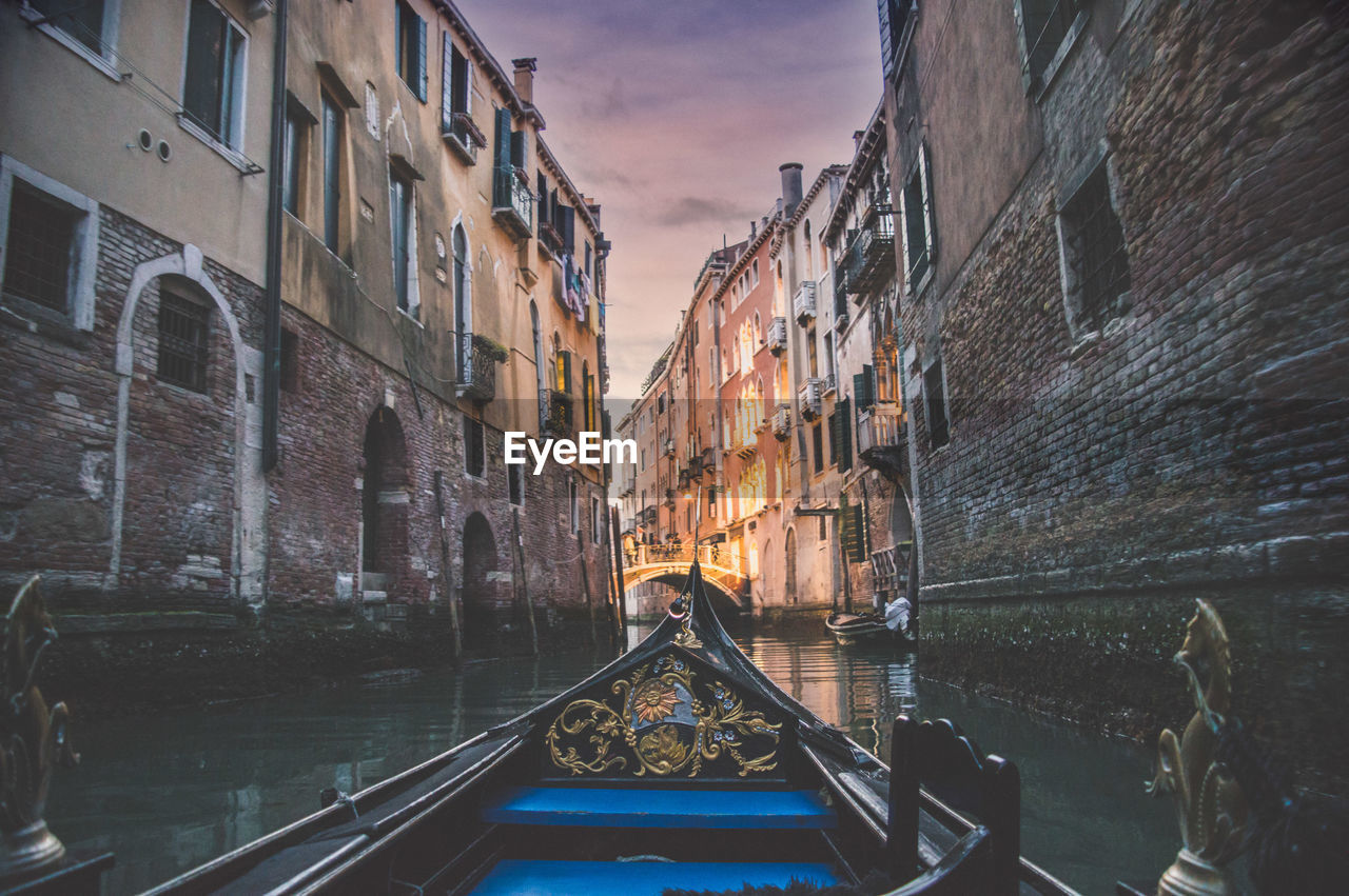 Gondola in canal amidst buildings during sunset