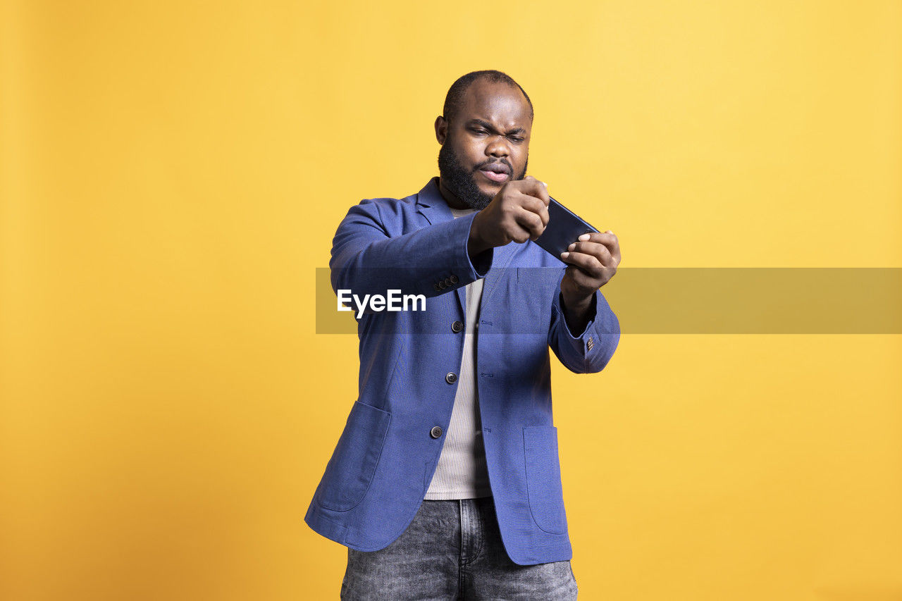 side view of young man using mobile phone against yellow background