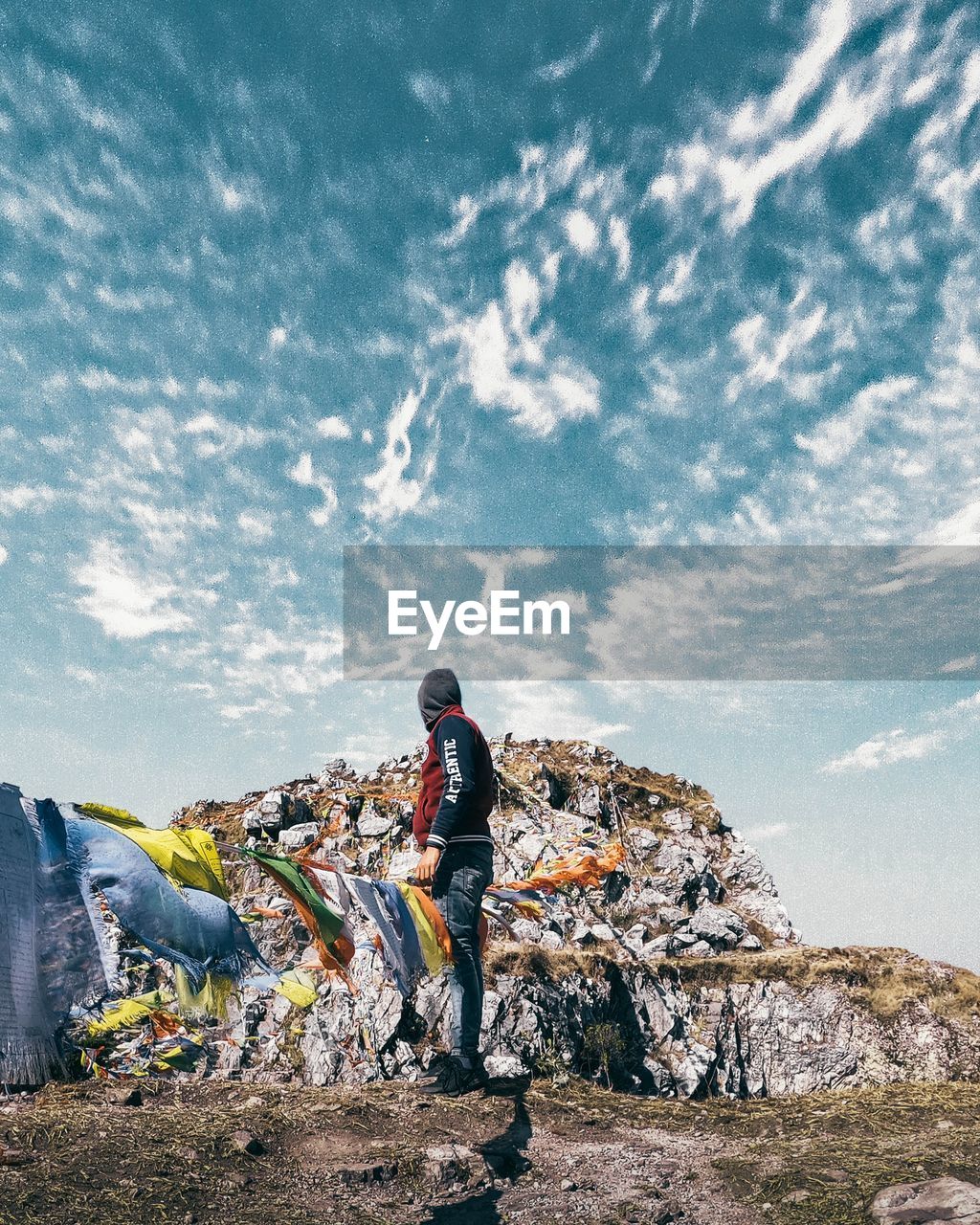 REAR VIEW OF MAN STANDING ON ROCK BY ROCKS AGAINST SKY