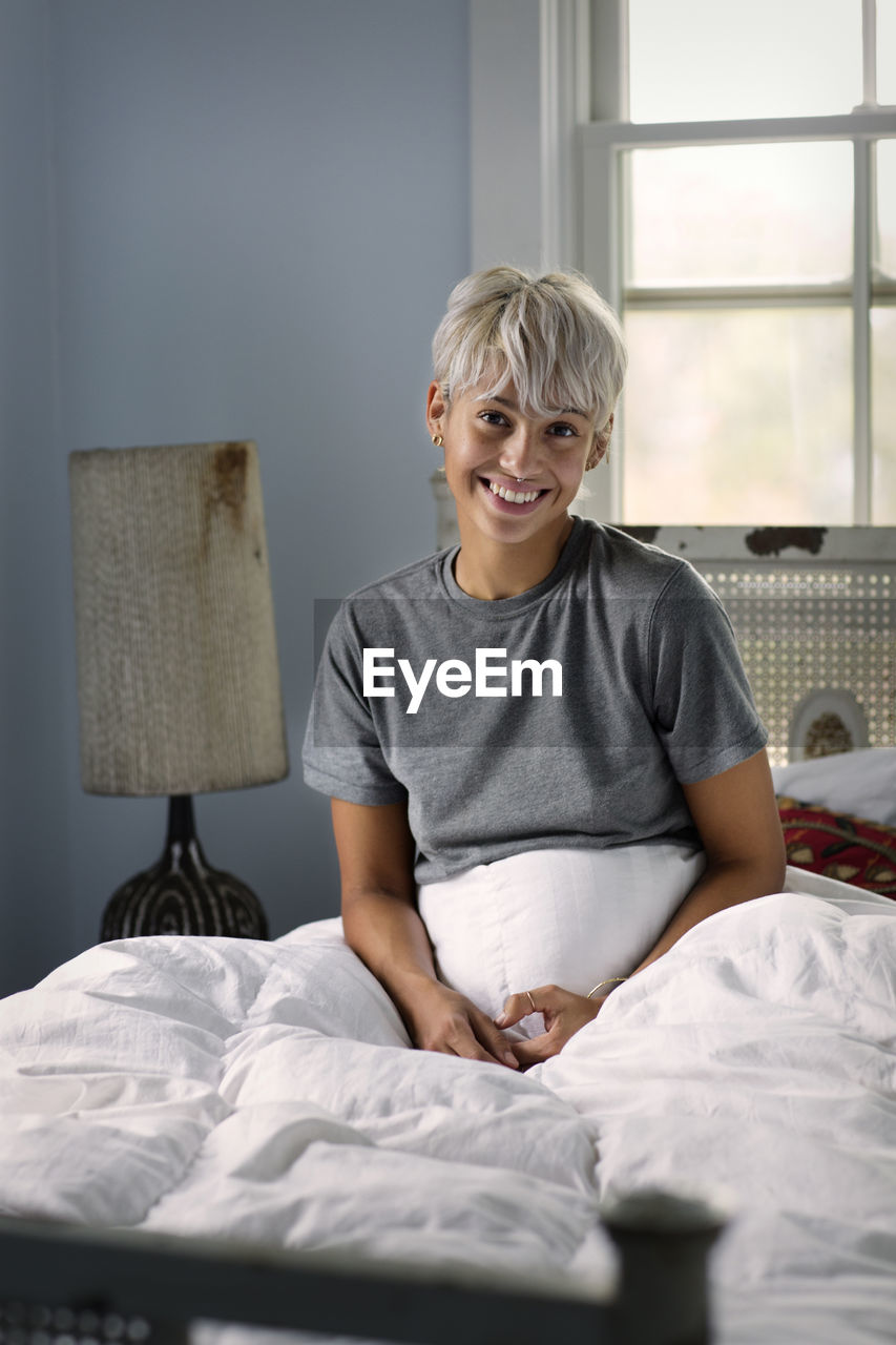 Portrait of happy young woman sitting on bed at home