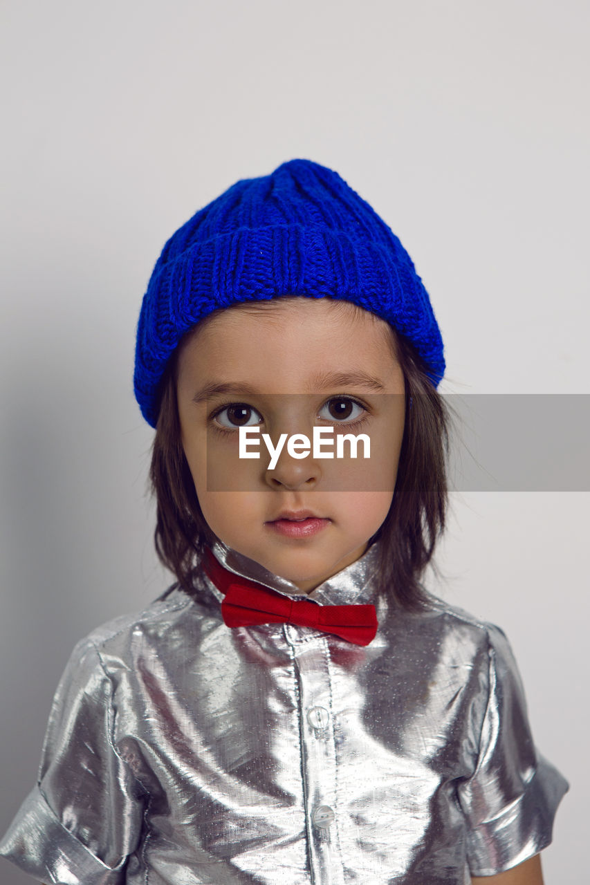 Portrait boy child in a blue knitted hat and silver shirt red bow tie on the background