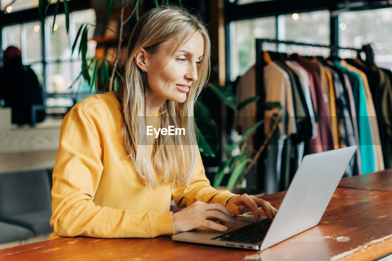 Saleswoman sitting at the counter working using a laptop.