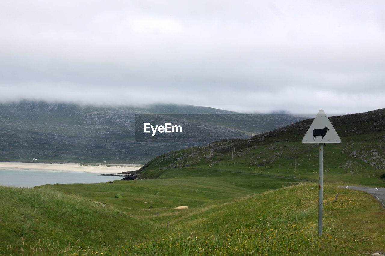 Road sign on landscape against cloudy sky