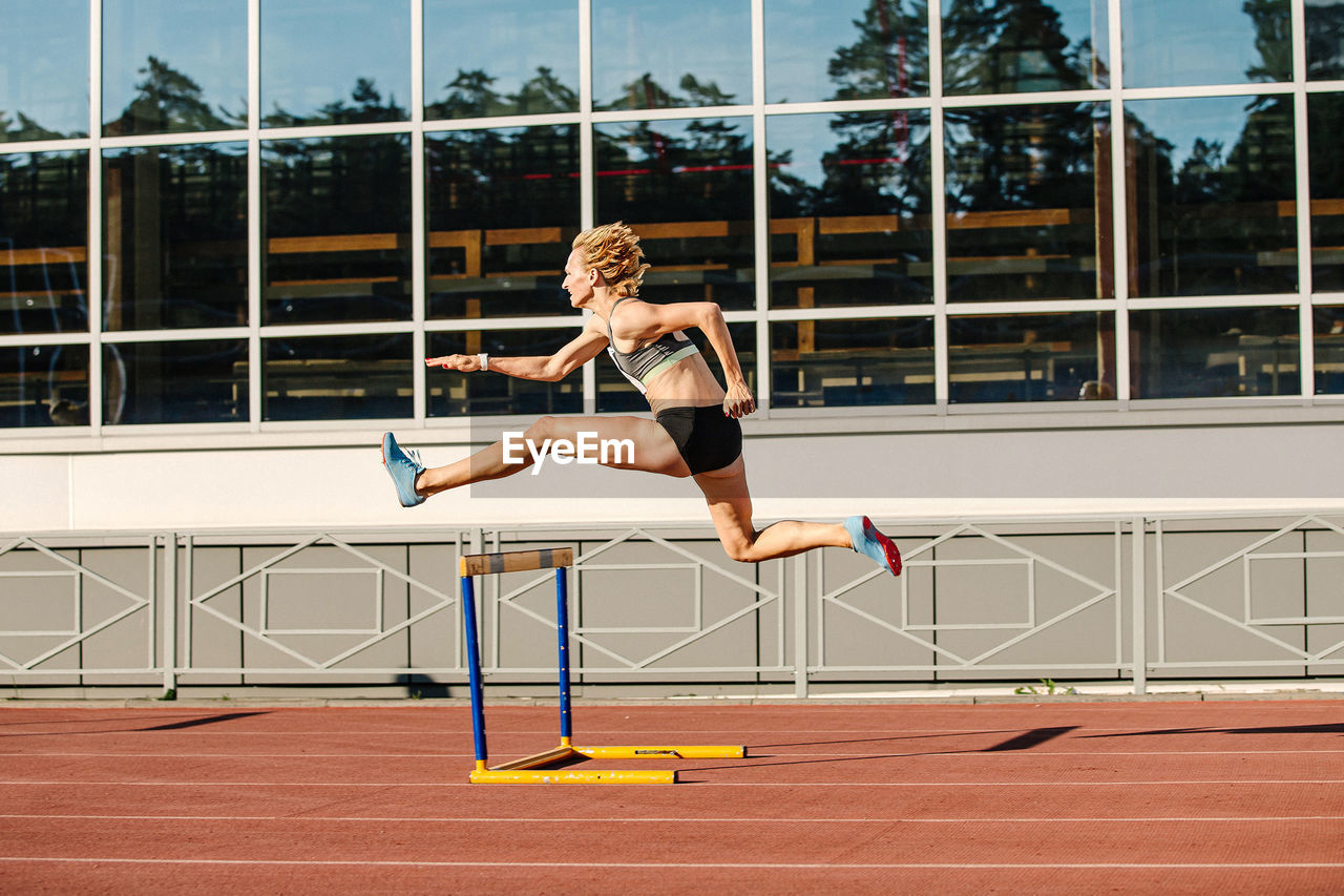 Woman athlete runnner running hurdles in summer athletics competition